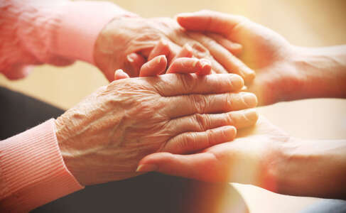 Old and young holding hands on light background, closeup